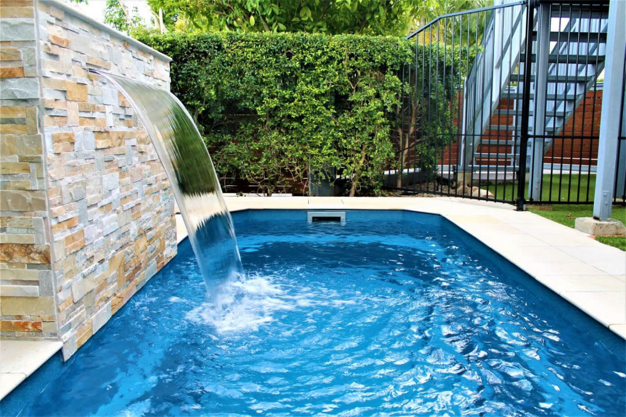 Modern bahçede yer alan taş duvarlı, şelale özellikli kompakt yüzme havuzu